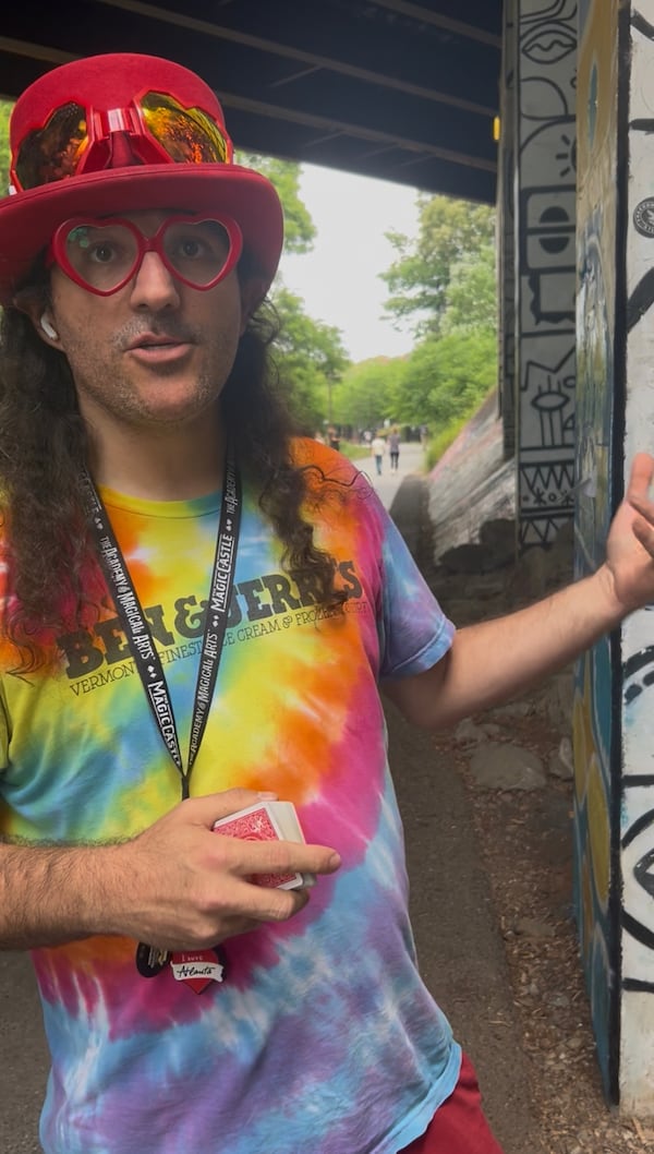 Tony Canas, also known as the Red Hat Magician, talks to a reporter about how he uses the Atlanta Trinket Trade to find new stickers on the Eastside Beltline. (Olivia Wakim/AJC)