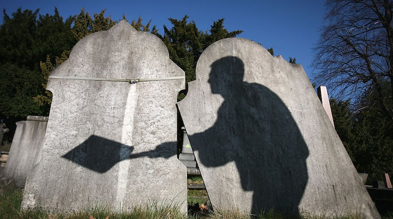 The shadow of a cemetery worker is cast on gravestones.