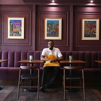 Chef Demetrius Brown poses for a portrait in the dining room of his new Heritage Supper Club. The walls are purple and loaded with art work.