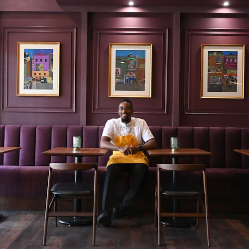 Chef Demetrius Brown poses for a portrait in the dining room of his new Heritage Supper Club. The walls are purple and loaded with art work.