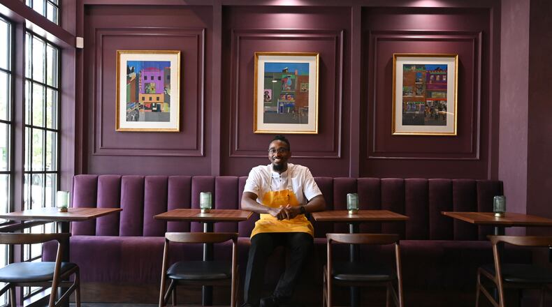 Chef Demetrius Brown poses for a portrait in the dining room of his new Heritage Supper Club. The walls are purple and loaded with art work.