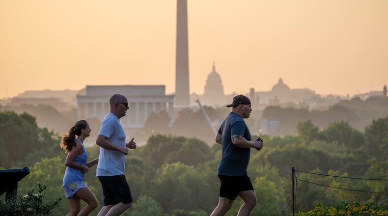 The Lincoln Memorial, Washington Monument, and U.S. Capitol are seen at dawn as joggers run past an overlook in Arlington, Va., Friday, July 3, 2026. (AP Photo/J. Scott Applewhite)