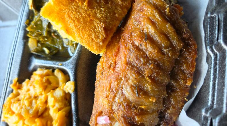 A close-up shot of a takeout container shows lemon pepper turkey wing, with sides of macaroni and cheese and collard greens tucked into the tray compartments. A square of cornbeard balances on top of the turkey wing.