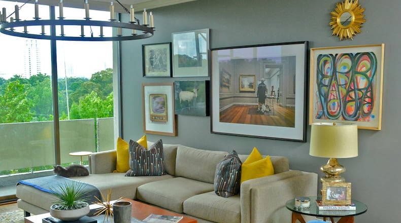 A gallery wall of art is assembled by Jason Moattar, a member of SCAD’s Atlanta Advisory Board, over a chaise sectional sofa from Room & Board in the living room with floor-to-ceiling windows. Blue velvet covers the two swivel chairs, purchased through R. Hughes at ADAC (Atlanta Decorative Arts Center), and brings out the blue tones in the yellow, gray and blue rug.(Christopher Oquendo Photography/www.christopheroquendophotography.com)