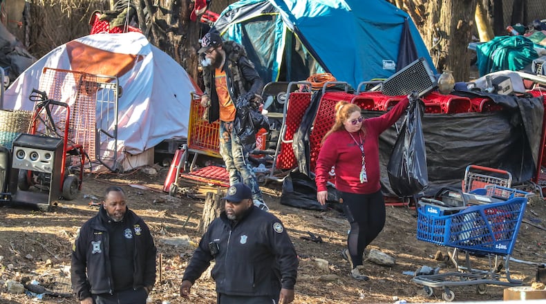 A member of the cleanup crew (right) helps a homeless man (left) gather his things. The city of Atlanta began a major new effort to clear out homeless people living under bridges, and encampments on Monday, Feb. 26, 2024. Georgia DOT employees began cleaning up and area supervised by a half dozen Atlanta police officers located in the 2600 block of Buford Hwy just north of Lenox Road in Atlanta where an encampment exists in an wooded area. The city has declined to share most details of the operation publicly, including which specific bridge areas will be targeted, how many people it anticipates moving, and what kind of housing and locations it might provide to those displaced.  (John Spink / John.Spink@ajc.com)