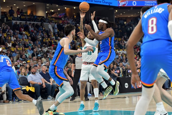 Memphis Grizzlies guard Ja Morant (12) shoots between Oklahoma City Thunder guard Luguentz Dort (5) and forward Chet Holmgren, center left, in the first half of Game 3 of an NBA first-round playoff series Thursday, April 24, 2025, in Memphis, Tenn. (AP Photo/Brandon Dill)