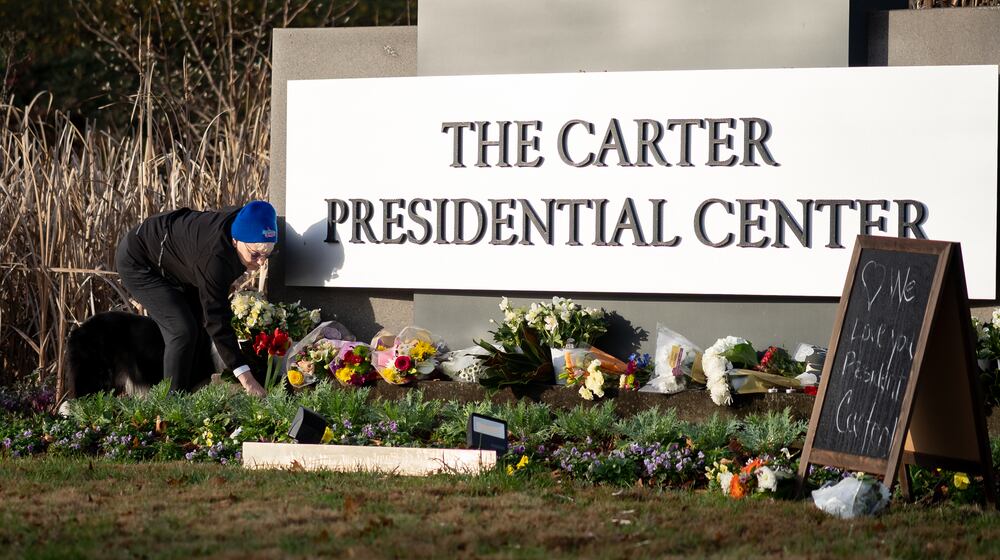 Laura Cole places amaryllis flowers on the sign at the Carter Presidential Center in Atlanta on Monday, December 30, 2024. (Ben Hendren for the Atlanta Journal-Constitution)