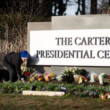 Laura Cole places amaryllis flowers on the sign at the Carter Presidential Center in Atlanta on Monday, December 30, 2024. (Ben Hendren for the Atlanta Journal-Constitution)