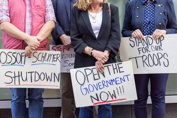 Supporters of Republican Derek Dooley, who is running for U.S. Senate, hold signs at a Dooley event outside incumbent Democrat Sen. Jon Ossoff’s office in Atlanta on Monday, October 13, 2025, keying on the government shutdown. (Arvin Temkar/AJC)