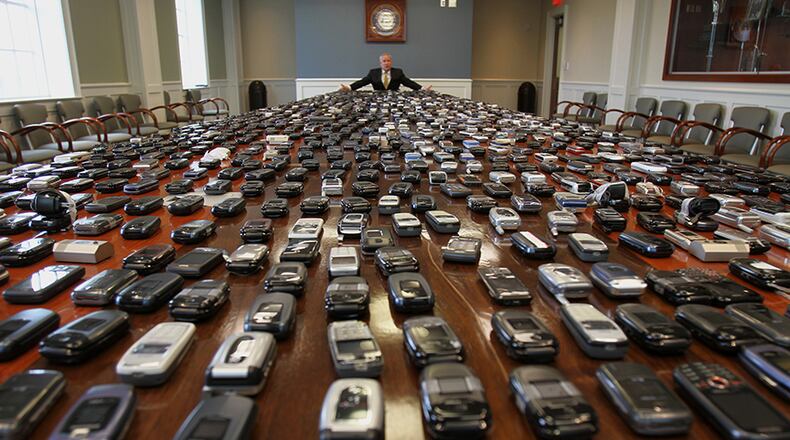 Dec. 20, 2011: Corrections Commissioner Brian Owens, sitting at a table holding more than 1,000 confiscated cellphones, talks about the threat and danger of the phones in prisons. (AJC file / Vino Wong)
