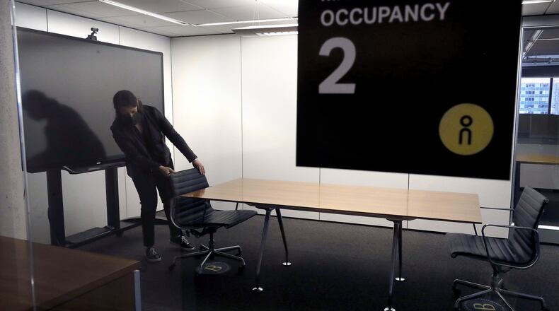 In this Thursday, May 7, 2020 photo, Vice President Rachel Zsembery at the design firm Bergmeyer, positions chairs in a conference room with a designated maximum occupancy of two people, at the firm’s offices, in Boston. Out of concern for the coronavirus Bergmeyer is restructuring the way its workspace is used, including reinstalling dividers on 85 desks at its Boston office that had been removed over the years. (AP Photo/Steven Senne)