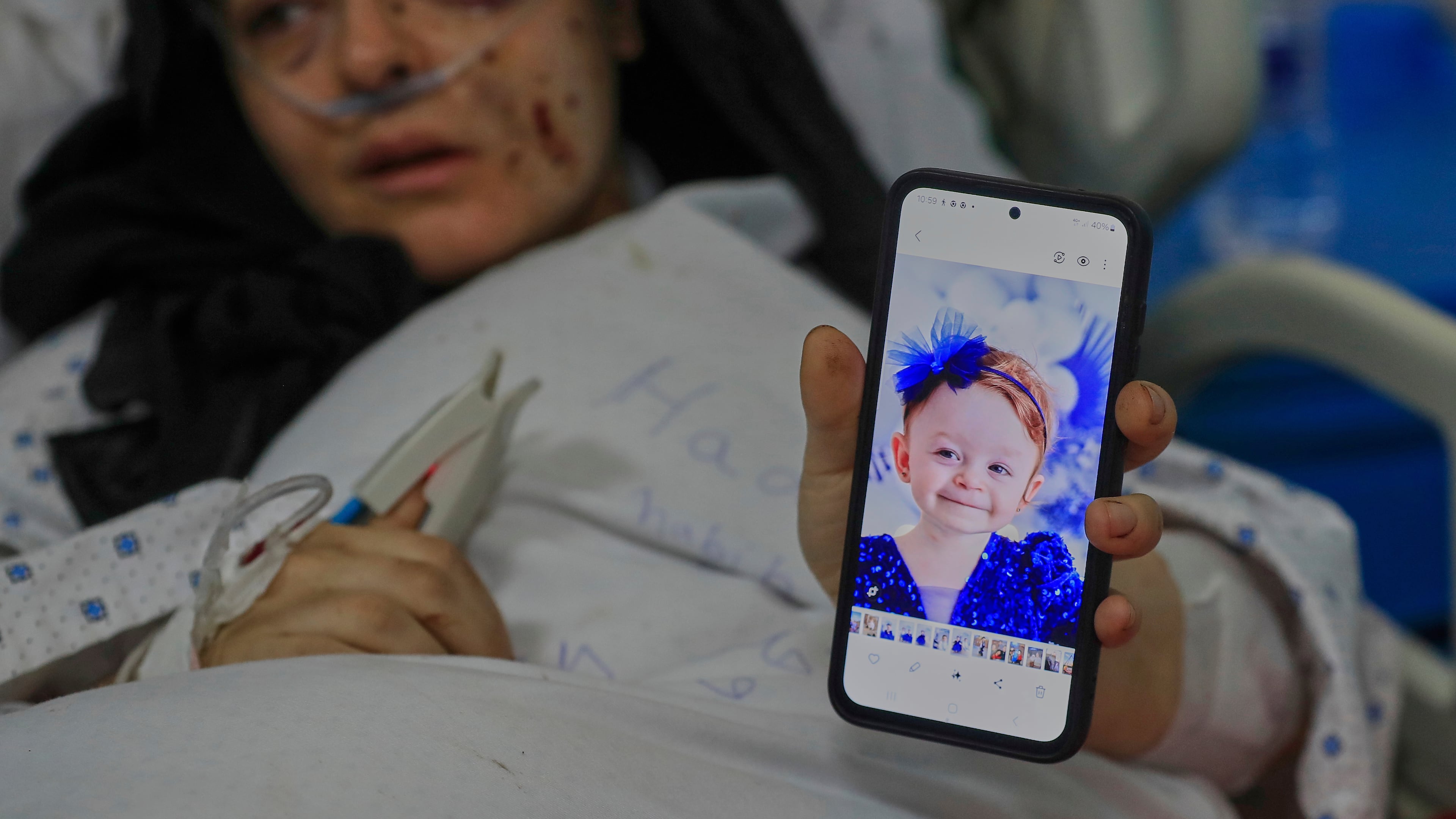 Amani Bazzi, who was injured Sunday in the town of Bint Jbeil, shows a portrait of one her three kids who were killed after an Israeli drone strike hit her family car, as she lies in Tibnin hospital, southern Lebanon, Monday, Sept. 22, 2025. (AP Photo/Mohammed Zaatari)