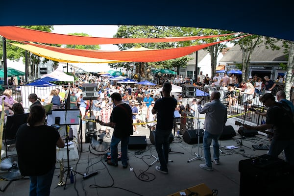A view of a crowd in a courtyard from the back of the stage while a band performs, silhouetted by the sun.