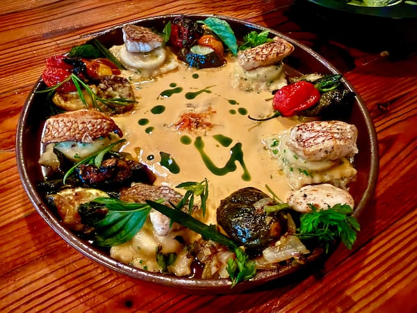 A large bowl of ravioli topped with vegetables, bright garnishes and a cream sauce.