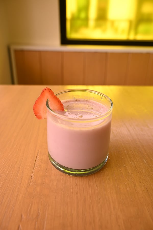 A short glass of thick, berry-colored lassi sits on a table.