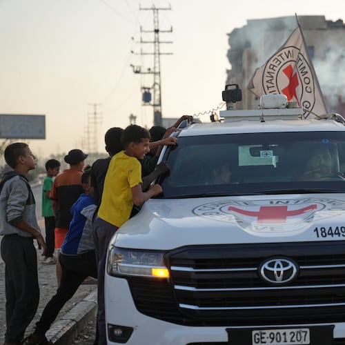 Palestinian kids look into a Red Cross vehicles carrying the bodies of two people believed to be deceased hostages handed over by Hamas make their way toward the Kissufim border crossing with Israel, to be transferred to Israeli authorities, in Deir al-Balah, central Gaza Strip, Thursday, Oct. 30, 2025. (AP Photo/Abdel Kareem Hana)