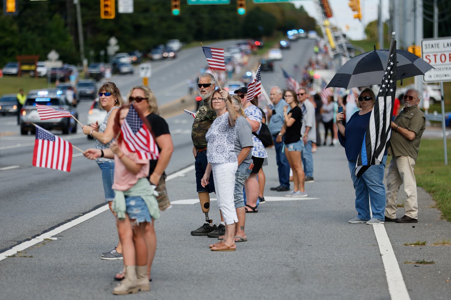 People stand by the Dallas Highway holding U.S. flags to pay respect to Marshall Samual Ervin Jr during the procession over Dallas Highway on Thursday, September 15, 2022. Miguel Martinez / miguel.martinezjimenez@ajc.com