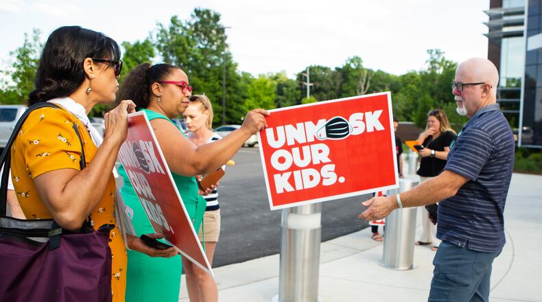Billy Cahill (far right) hands a woman his "unmask our kids" sign to pose for a photo outside of the Cobb County School District office on Thursday, May 20, 2021, in Marietta, Georgia . Many community members waited in line to speak at the school board meeting to voice their support for unmasking. CHRISTINA MATACOTTA FOR THE ATLANTA JOURNAL-CONSTITUTION