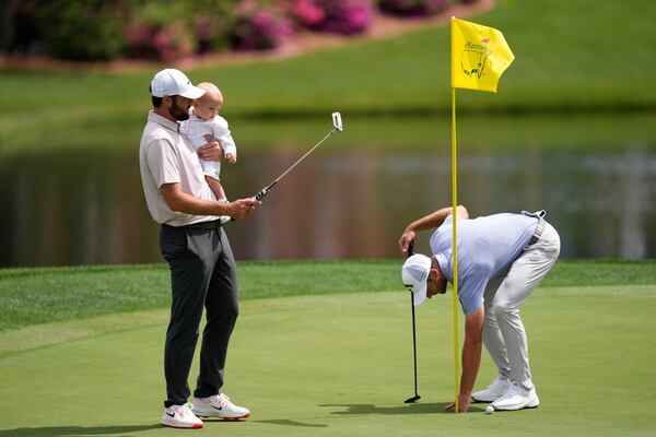 Scottie Scheffler holds his child Bennett as Sam Burns removes his ball on the first hole during the par-3 contest at the Masters golf tournament, Wednesday, April 9, 2025, in Augusta, Ga. (AP Photo/Ashley Landis)