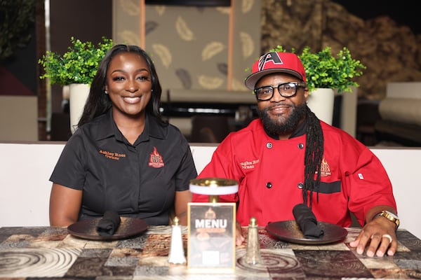 A woman (left) and man sit next to each other wearing branded chef shirts for their restaurant, Beyond BBQ.