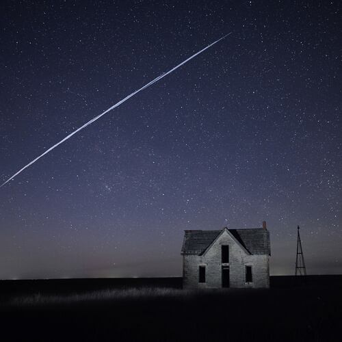FILE - In this long exposure photo, a string of SpaceX StarLink satellites passes over an old stone house near Florence, Kan., on May 6, 2021. (AP Photo/Reed Hoffmann, File)