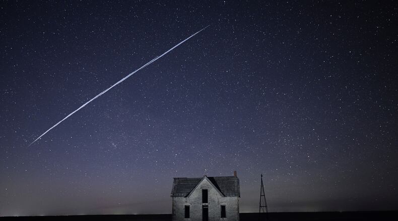 FILE - In this long exposure photo, a string of SpaceX StarLink satellites passes over an old stone house near Florence, Kan., on May 6, 2021. (AP Photo/Reed Hoffmann, File)