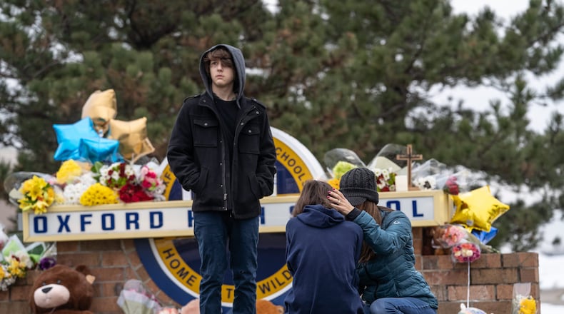 People comfort each other while visiting a memorial being built at an entrance to Oxford High School on December 1, 2021, following an active shooter situation at Oxford High School that left four students dead and multiple others with injuries. (Ryan Garza/Detroit Free Press/TNS)