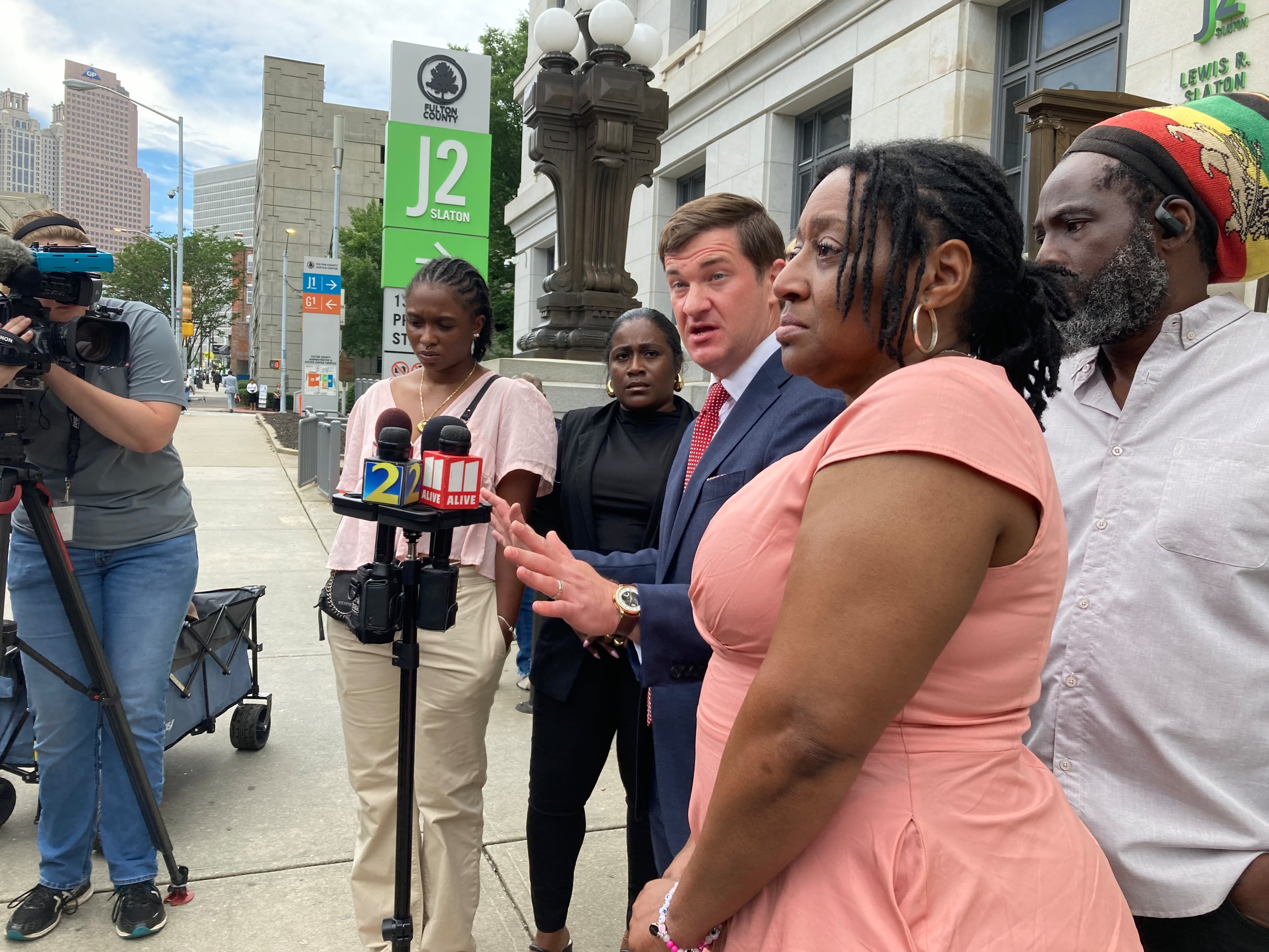 Parker Miller (center, in suit), an attorney for Mari Creighton's parents, speaks to reporters outside the Fulton County Courthouse in June 2024. With Parker are Creighton's parents, Tracey Eason (center foreground) and Juan Umberto Creighton (right), Mari's best friend, Bryanna Davis (left center), and Mari's sister, Tiffany Eason (center, wearing black). (Rosie Manins/AJC 2024)