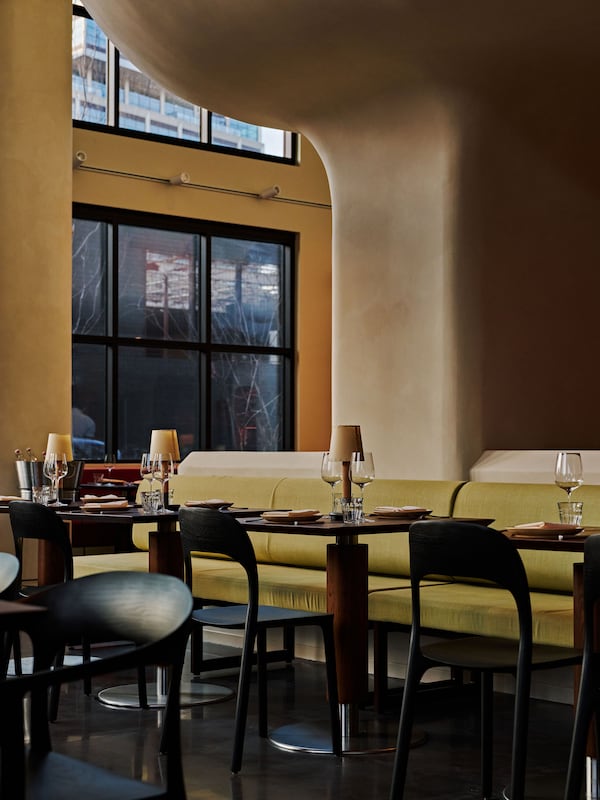 A modern restaurant dining room without any people and a tall, curving, white stucco wall in the background.