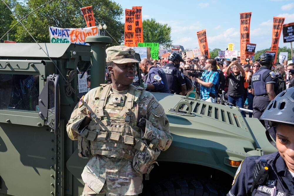 Washington Metropolitan Police officers and military police soldiers with the District of Columbia National Guard kept watch Saturday as activists protested the federal takeover of policing there.