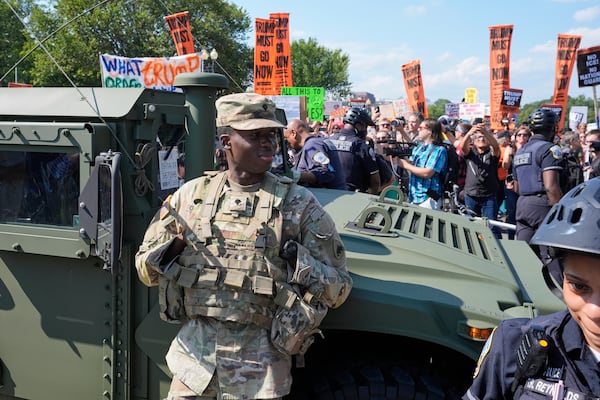 Washington Metropolitan Police officers and military police soldiers with the District of Columbia National Guard kept watch Saturday as activists protested the federal takeover of policing there.