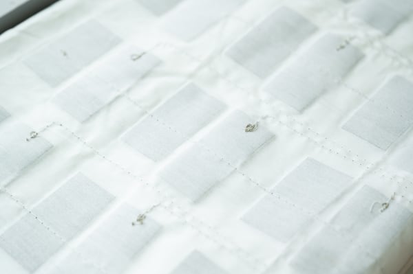 A sheet embedded with lightweight fabric sensors sits atop the crib mattress and under the fitted crib sheet. The sensors, which are flexible and reusable after being sanitized, send data to an app that monitors a patient’s condition. (Courtesy of Georgia Tech) 