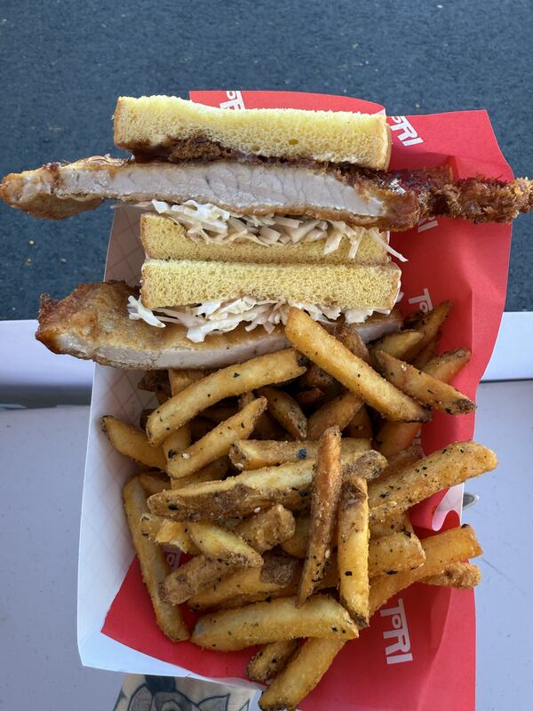 A top-down view of a pork katsu sandwich cut in half alongside seasoned french fries in a red paper-lined paper boat tray.