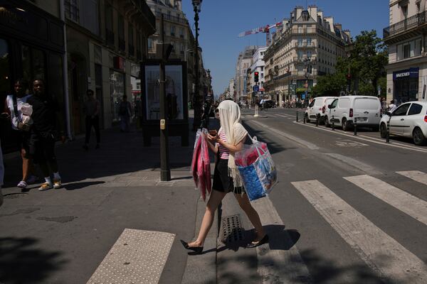 A woman protects her head during a heat wave, Monday, June 30, 2025 in Paris. (AP Photo/Christophe Ena)