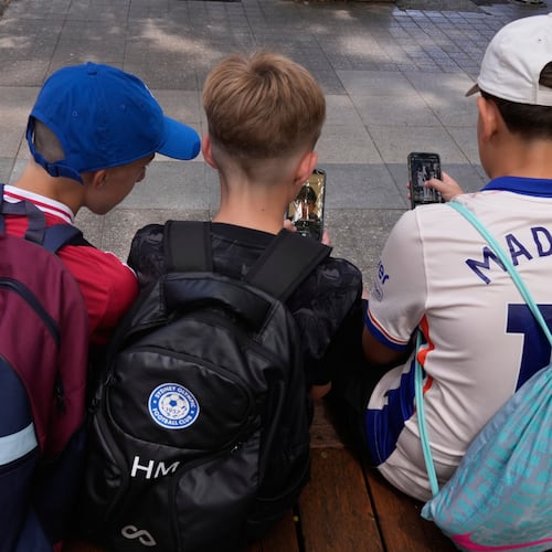 FILE - Three boys use their phones while sitting outside a school in Sydney, Monday, Dec. 8, 2025. (AP Photo/Rick Rycroft, File)