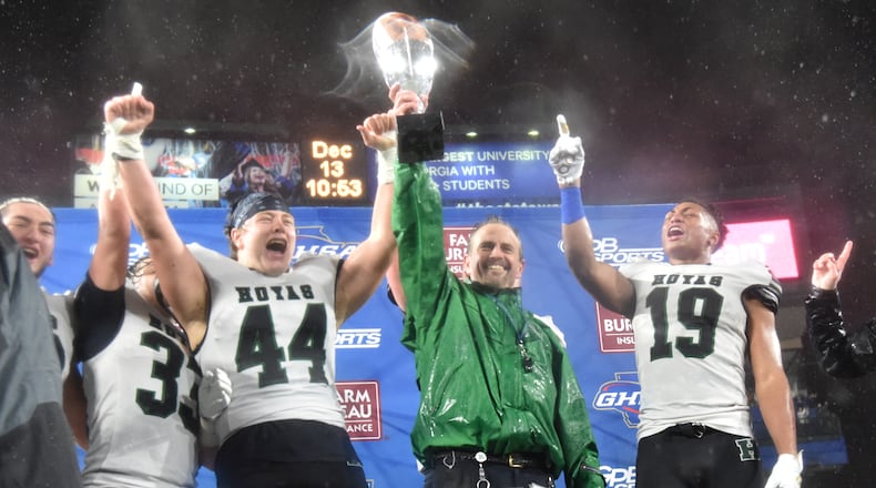 Harrison head coach Matt Dickmann and player Mason Bollin (44) hold their championship trophy after the AAAAAA state championship game at Georgia State Stadium on Friday, December 13, 2019. Harrison won 20-7 over Allatoona. (Hyosub Shin / Hyosub.Shin@ajc.com)