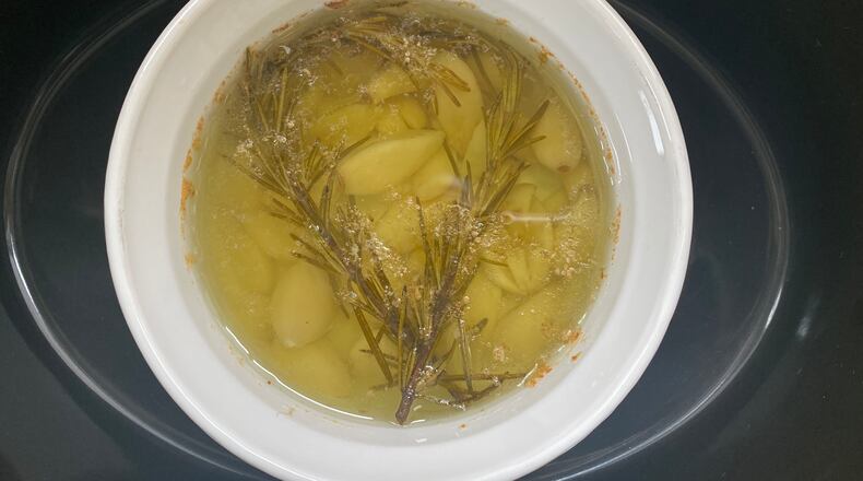 Garlic confit, whose recipe includes fresh rosemary, comes together easily in the slow cooker. The roasted garlic flavor makes any savory dish worthy of a holiday. (Kellie Hynes for The Atlanta Journal-Constitution)