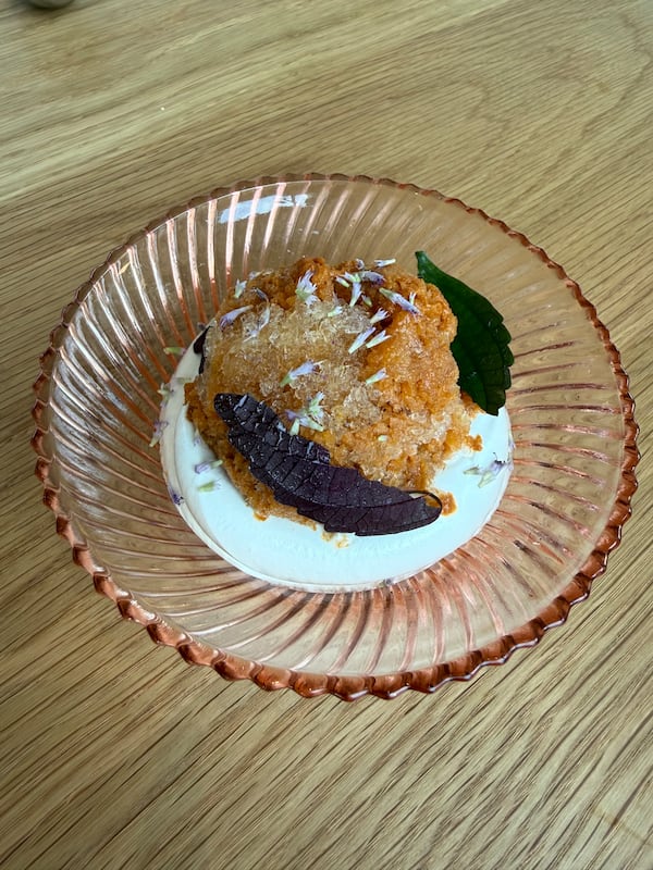 A small dish contains peach granita on top of what looks like a circle of marshmallow fluff. It is garnished with fresh clover.