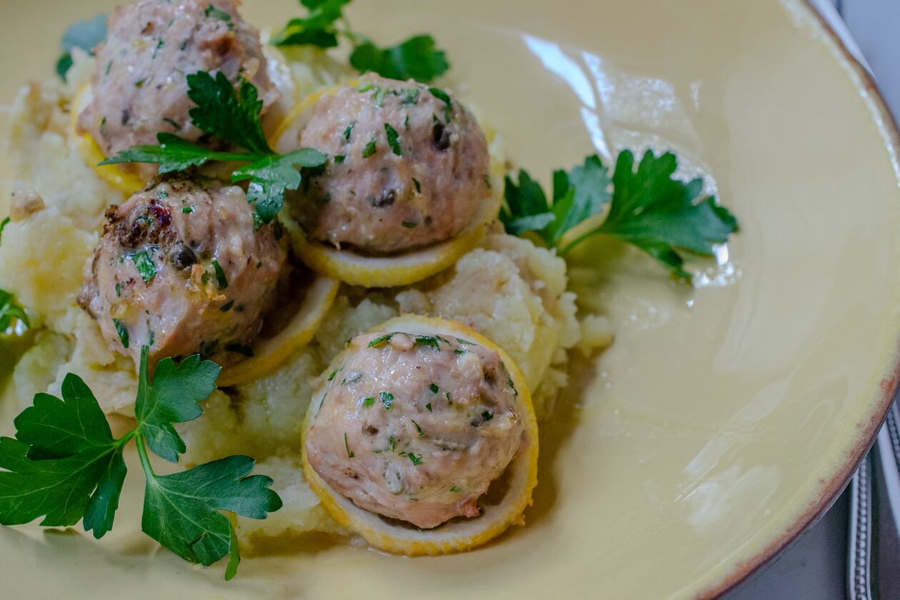 Baked chicken piccata meatballs with sliced lemon, fresh parsley and extra virgin olive oil. (Virginia Willis for The Atlanta Journal-Constitution)