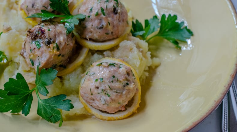 Baked chicken piccata meatballs with sliced lemon, fresh parsley and extra virgin olive oil. (Virginia Willis for The Atlanta Journal-Constitution)