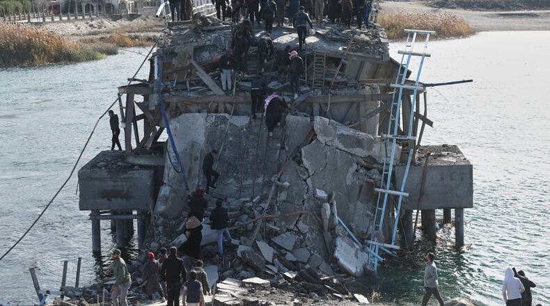 People climb over the damaged Al-Rashid Bridge, with some crossing on foot, after it was destroyed as Kurdish-led Syrian Democratic Forces withdrew, a day after Syrian government forces took control of the area on the outskirts of Raqqa, northeastern Syria, Monday, Jan. 19, 2026. (AP Photo/Ghaith Alsayed)