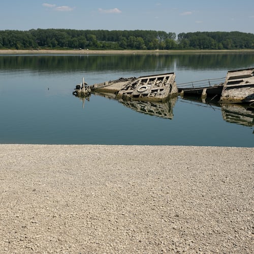 A man walks on the sandbank by the wreckage of a WWII German warship, emerged due to the drought, in front of Djerdap II, a large dam on the Danube River, between Romania and Serbia, near Prahovo, Serbia, Tuesday, Aug. 4, 2026. (AP Photo/Darko Vojinovic)