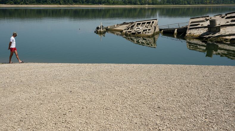 A man walks on the sandbank by the wreckage of a WWII German warship, emerged due to the drought, in front of Djerdap II, a large dam on the Danube River, between Romania and Serbia, near Prahovo, Serbia, Tuesday, Aug. 4, 2026. (AP Photo/Darko Vojinovic)