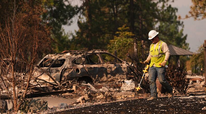A worker with Avista moves through a property after a wildfire hit the northern part of Spokane, Wash., Monday, Aug. 3, 2026. (AP Photo/Lindsey Wasson)