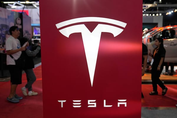 People pass by a Tesla sign at the Manila International Auto Show in Pasay city, Philippines Friday, April 11, 2025. (AP Photo/Aaron Favila)