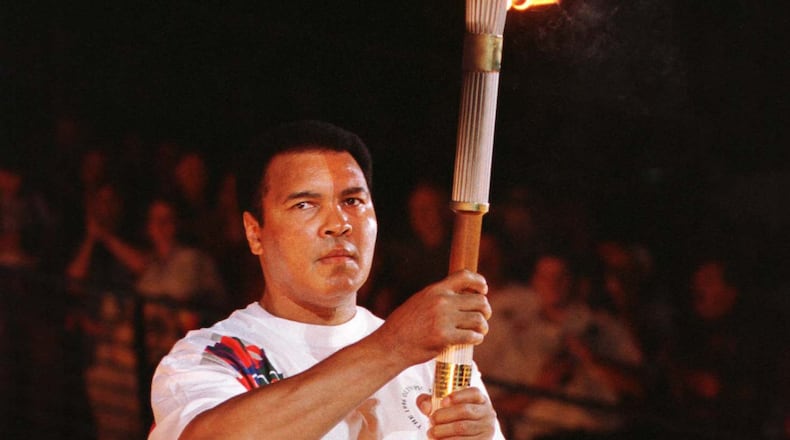 Former boxer Muhammad Ali, a Gold Medal winner in boxing in the 1960 Olympics when his name was Cassius Clay, holds up the torch prior to lighting a device that would carry the flame up the cauldron, during the opening ceremonies of the XXVI Centennial Olympic Games in Atlanta, July 19. - RTXGNH6