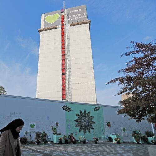 FILE - A woman passes a construction wall with written messages near Grenfell Tower in London, Wednesday, Oct. 30, 2019. (AP Photo/Frank Augstein, file)