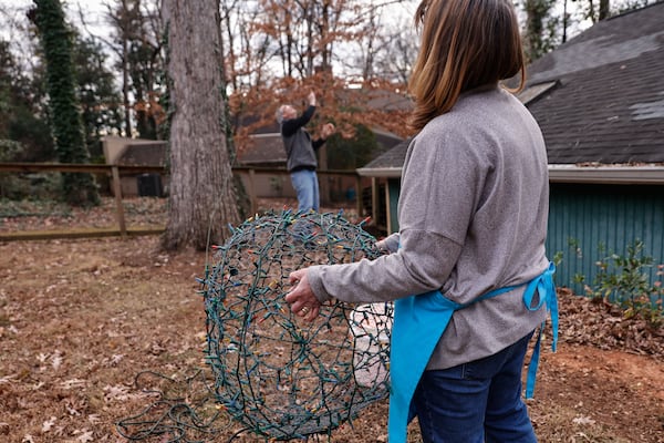 Mary Rigger holds a Christmas sphere light as her husband Don pulls it up into a tree in the backyard of their Decatur home. (Natrice Miller/AJC)