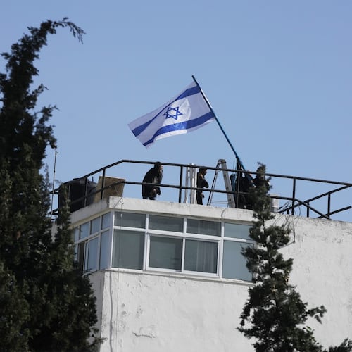 Israeli police and officials hang an Israeli flag on the compound of the United Nations agency for Palestinian refugees in East Jerusalem, after Israel police forcibly entered the compound, Monday, Dec. 8, 2025. (AP Photo/Mahmoud Illean)