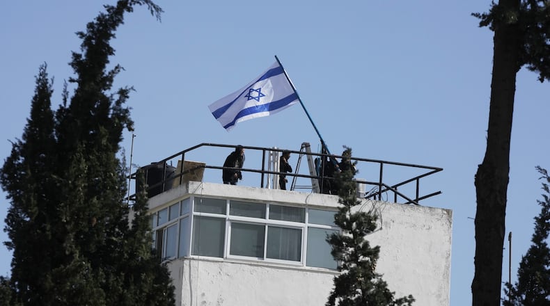 Israeli police and officials hang an Israeli flag on the compound of the United Nations agency for Palestinian refugees in East Jerusalem, after Israel police forcibly entered the compound, Monday, Dec. 8, 2025. (AP Photo/Mahmoud Illean)